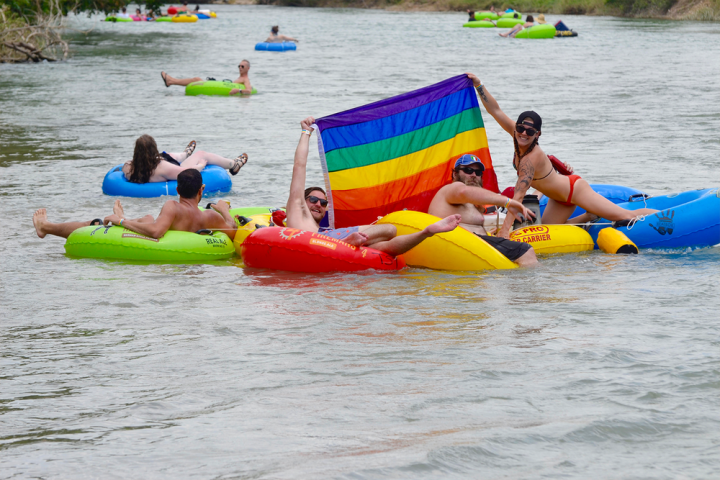 a group of people floating down a river holding up a pride flag