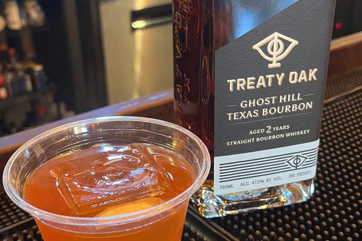 a drink in a cup next to a bottle of bourbon